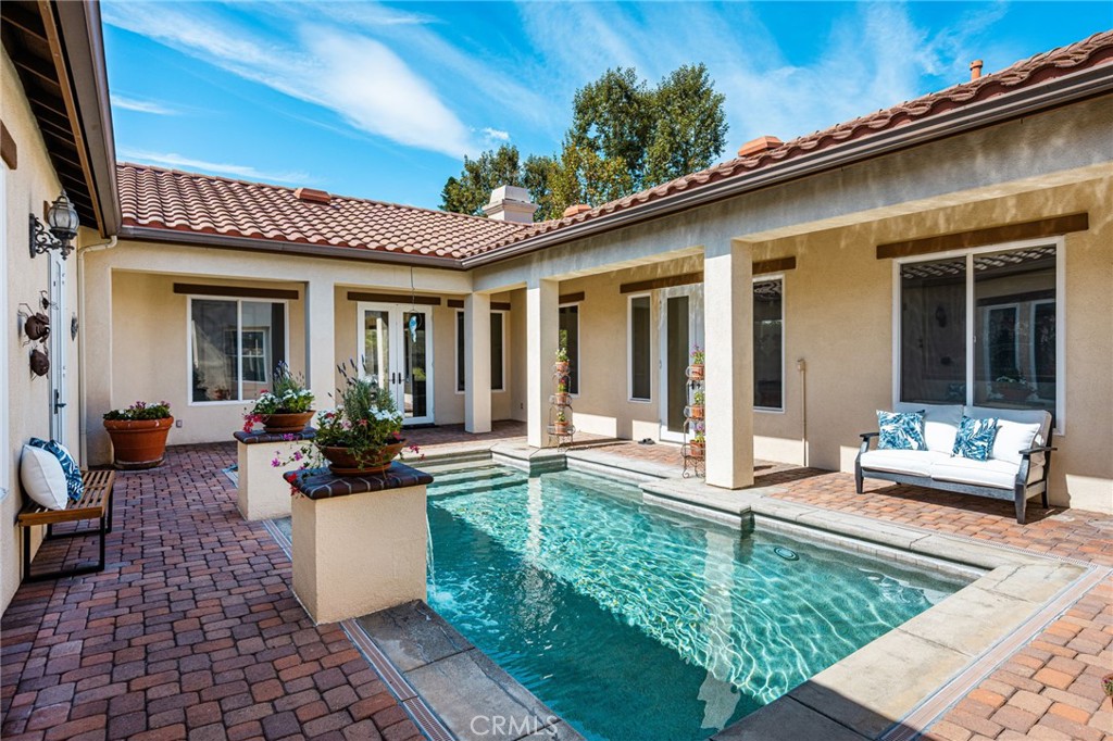 Courtyard pool surrounded by brick paving, stucco walls, and outdoor seating.