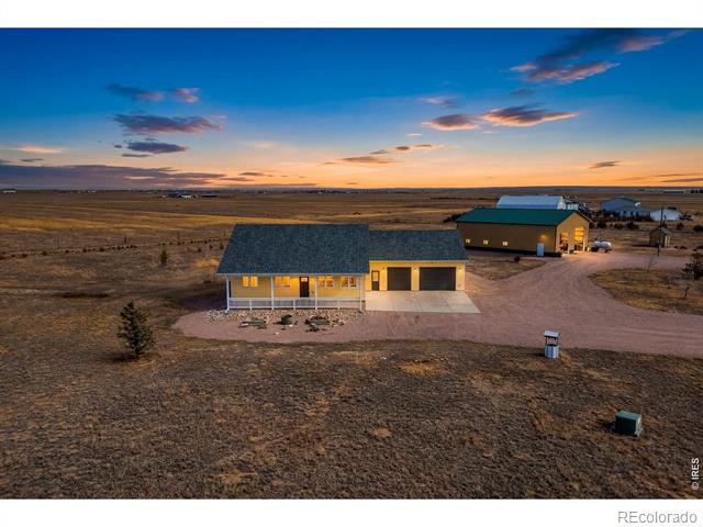 Aerial view of a home with an attached garage and detached outbuilding on open land at dusk.