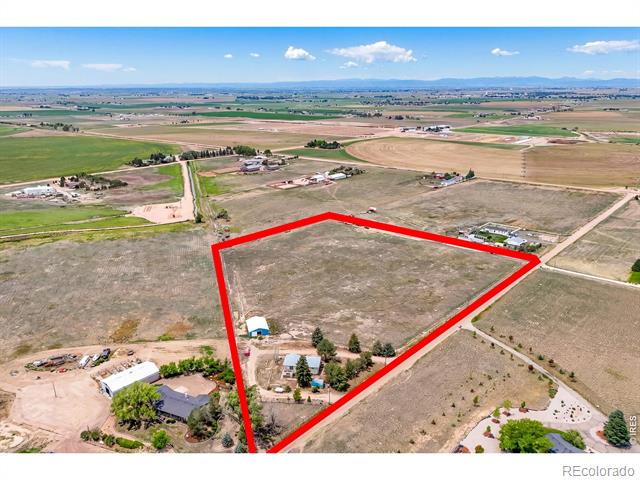 A rural parcel outlined in red, with scattered buildings near its edge and distant mountains.