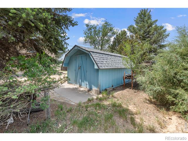Blue detached shed with double doors and a gray shingle roof among trees.