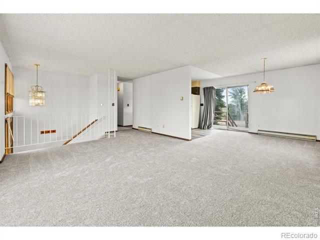 Vacant living room with gray carpet, stair railing, and sliding glass doors.