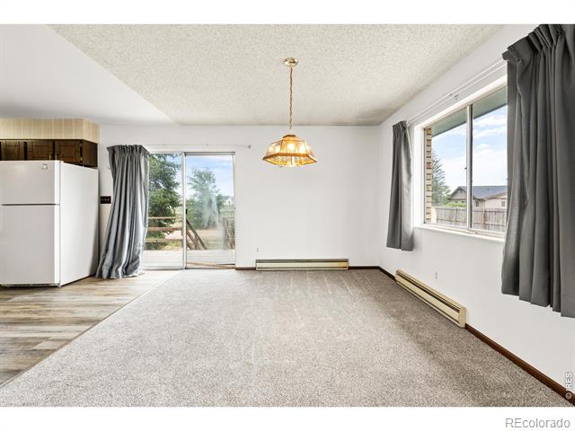 Empty carpeted living area with a hanging light, large curtained windows, and a sliding door to the deck.