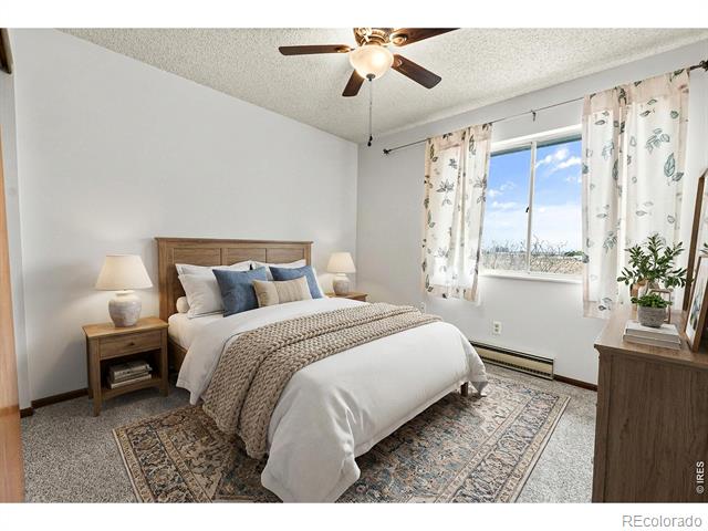 Bedroom with a wooden bed, patterned curtains, ceiling fan, and window overlooking open land.