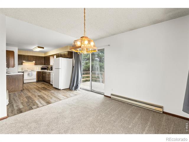 Unfurnished dining area with a lit chandelier, open kitchen, and sliding glass door.