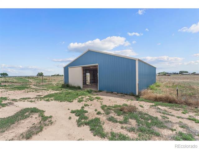 Blue metal outbuilding with an open doorway on flat, sparsely vegetated land.