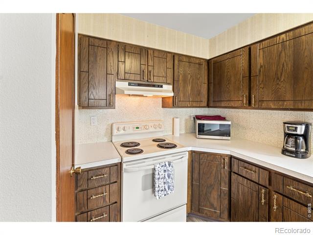 Kitchen with dark wood cabinets, white countertops, and a white electric range.