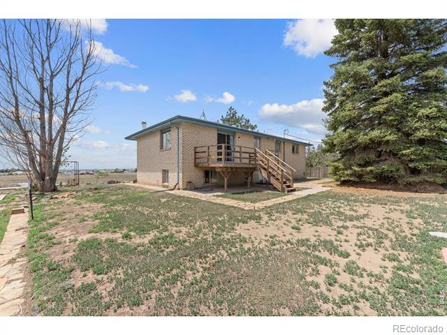 Tan brick house with a raised wooden deck and stairs on a sparse rural lot.