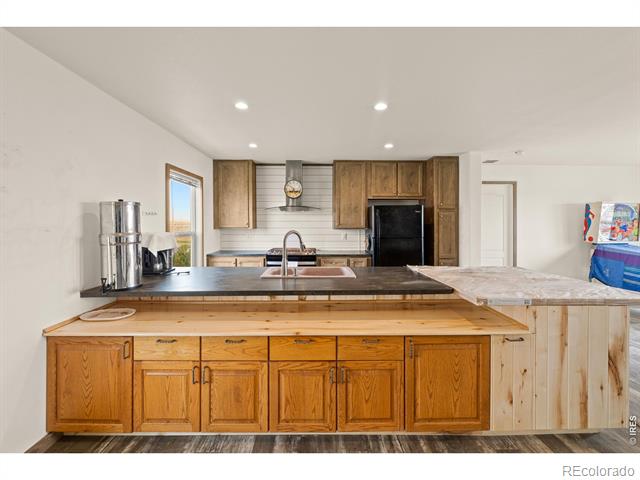 Kitchen with honey-colored wood cabinetry, dark countertops, a large island, and stainless appliances.