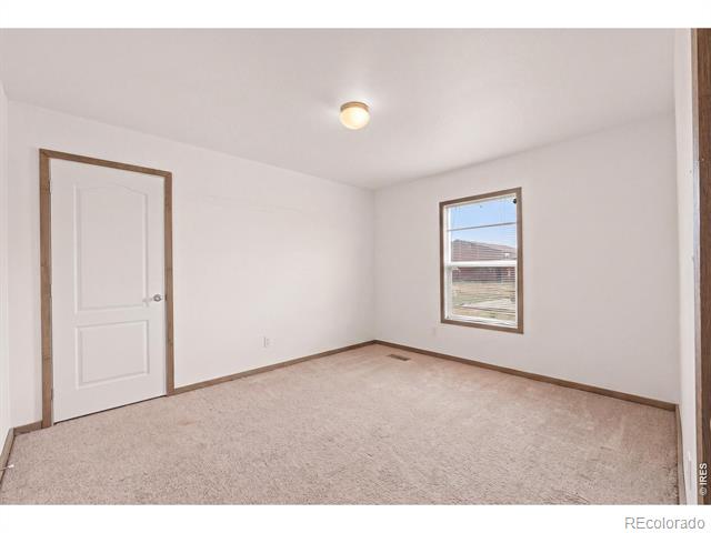 Empty bedroom with beige carpet, wood trim, and a window overlooking the yard.