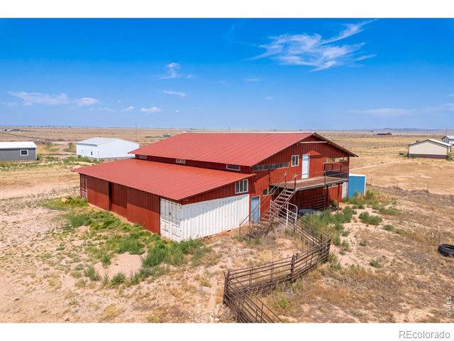 Red-roofed rural property with exterior stairs and fencing, surrounded by dry open land.