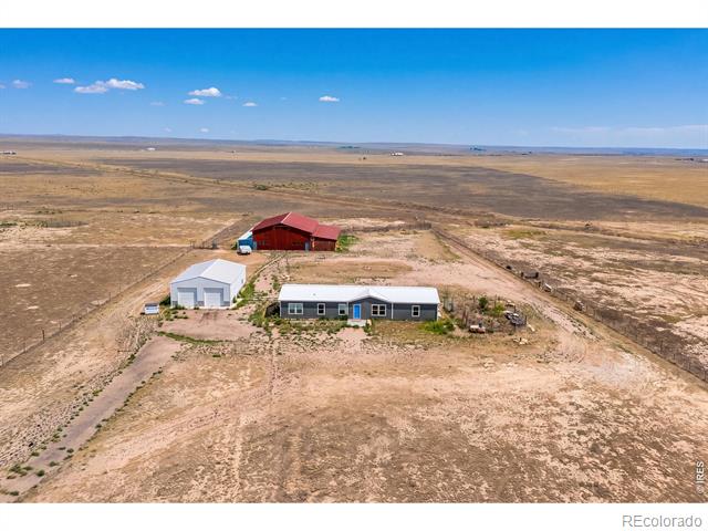 Aerial view of a rural property with a home, red barn, white outbuilding, and expansive dry grassland.