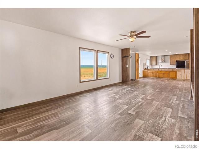 Unfurnished open-plan living area and kitchen with plank flooring, wood cabinets, and views of open fields.