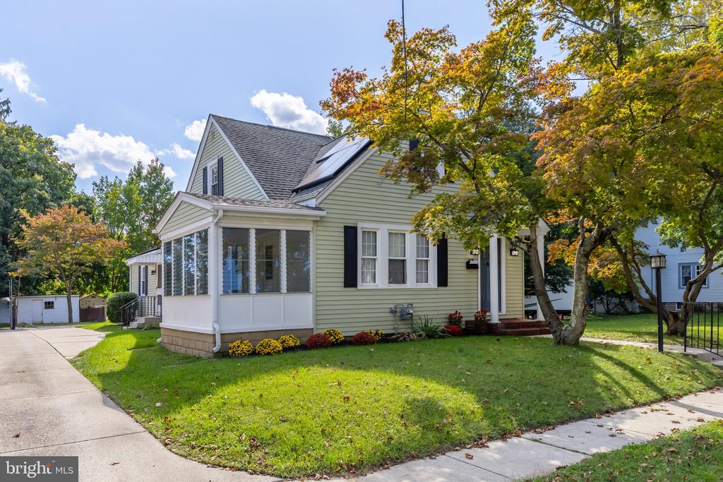 Sage-green house with a white enclosed porch, black shutters, and autumn trees.