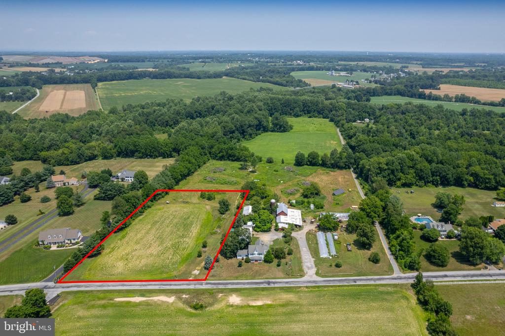 Aerial view of a red-outlined vacant parcel beside a road, surrounded by fields and wooded areas.