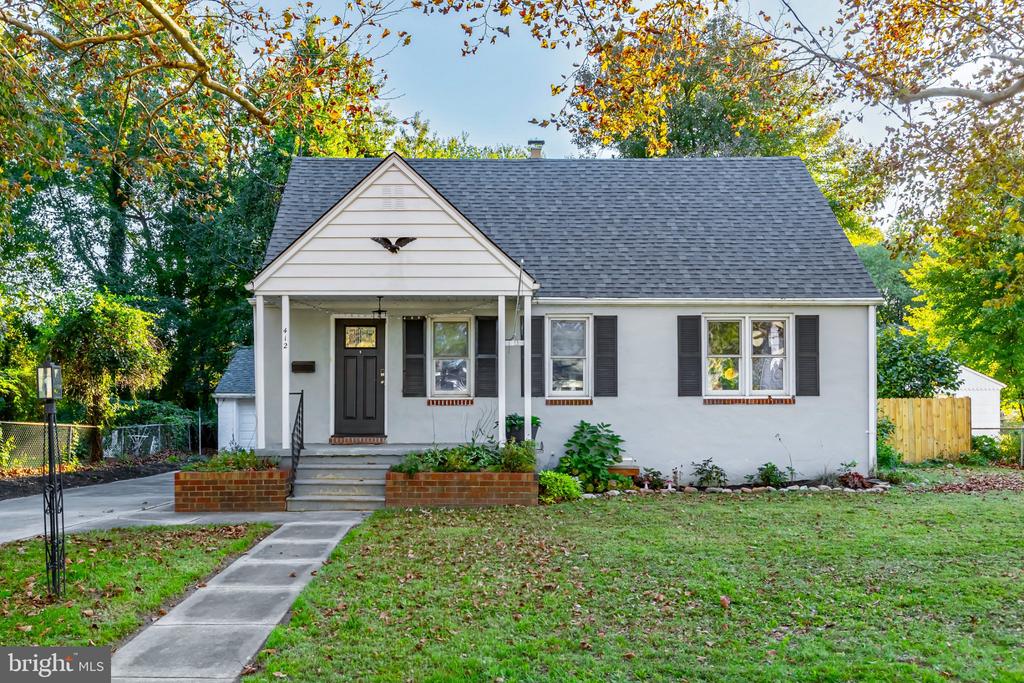 White ranch-style home with dark shutters, front porch, and mature autumn trees.
