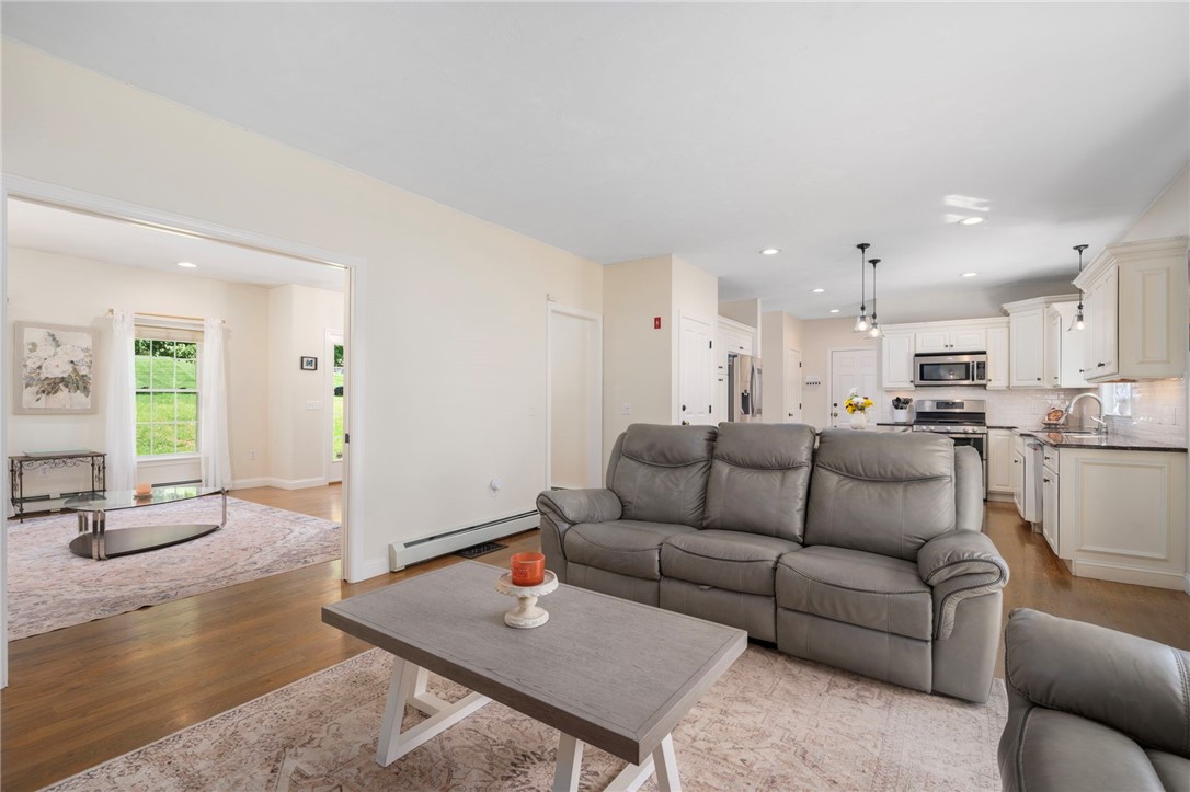 Living room with a gray sectional sofa, open to a bright white kitchen and dining area.