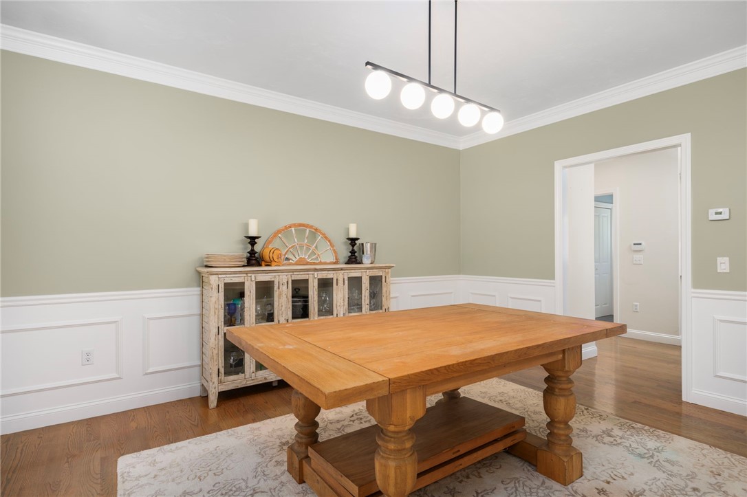 Dining room with a large wooden table, glass-front sideboard, and white paneled wainscoting.