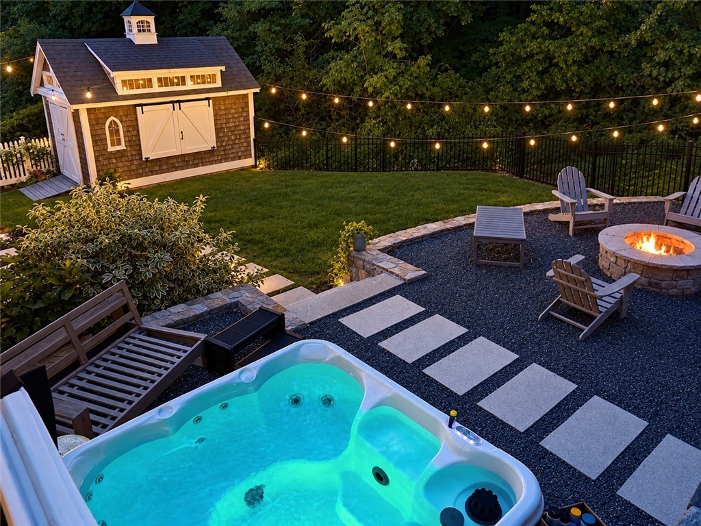 Backyard hot tub beside a fire pit, seating area, and illuminated garden shed.