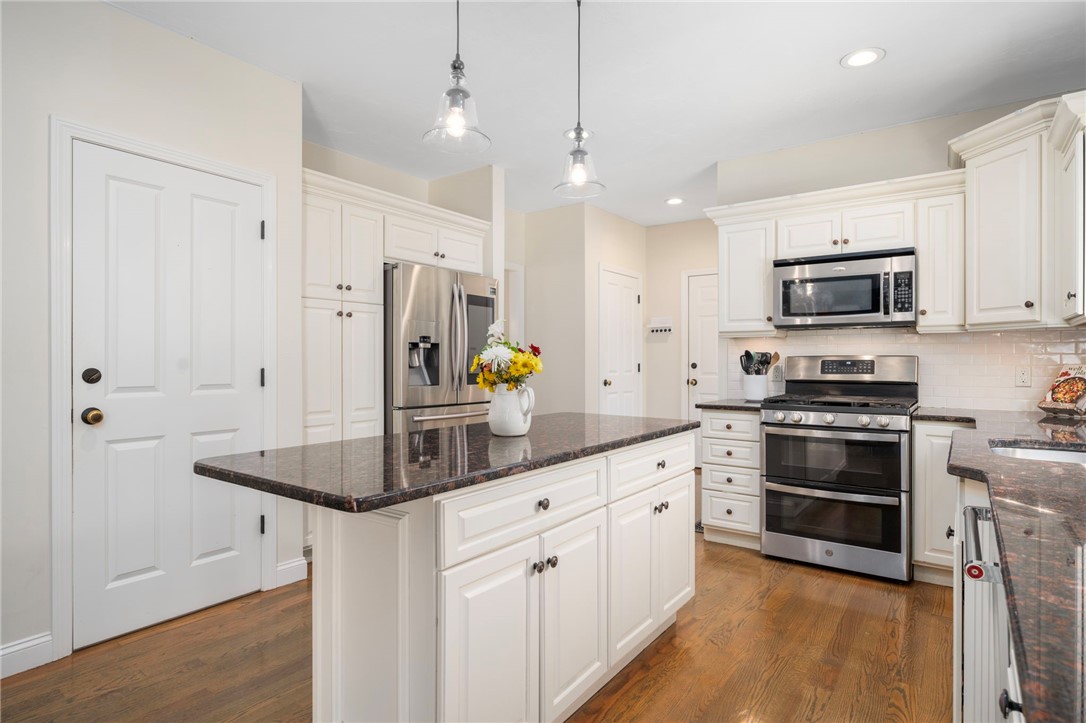 Bright kitchen with white cabinets, a dark stone island, stainless steel appliances, and hardwood floors.