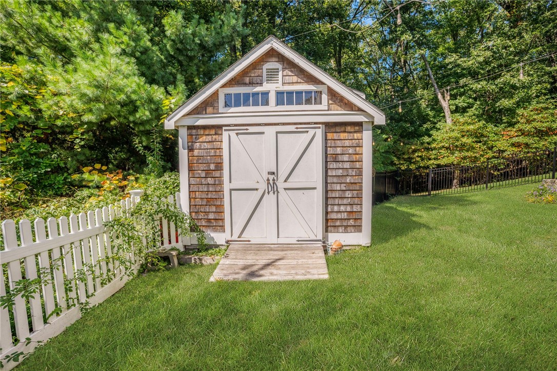 Backyard shed with weathered shingles, white double doors, and surrounding lawn and trees.