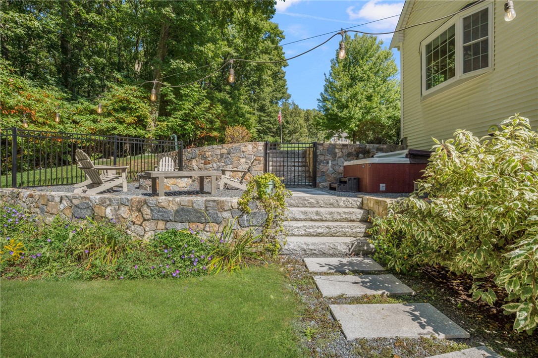 Stone patio with hot tub, lounge chairs, garden steps, and overhead string lights.