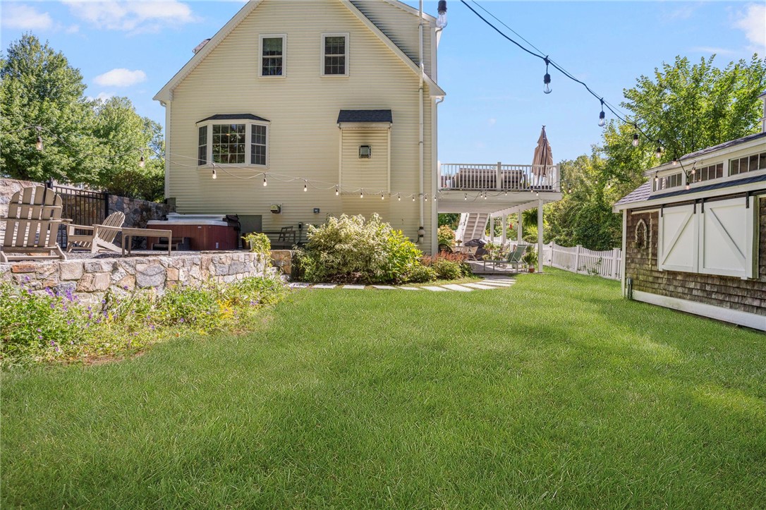 Rear yard of a two-story home with a raised deck, stone patio seating, and a detached shed.
