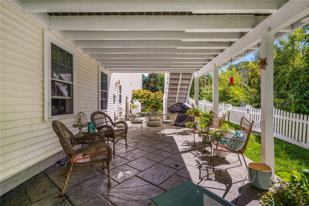Covered stone patio with wicker seating, a dining set, and a fenced garden.