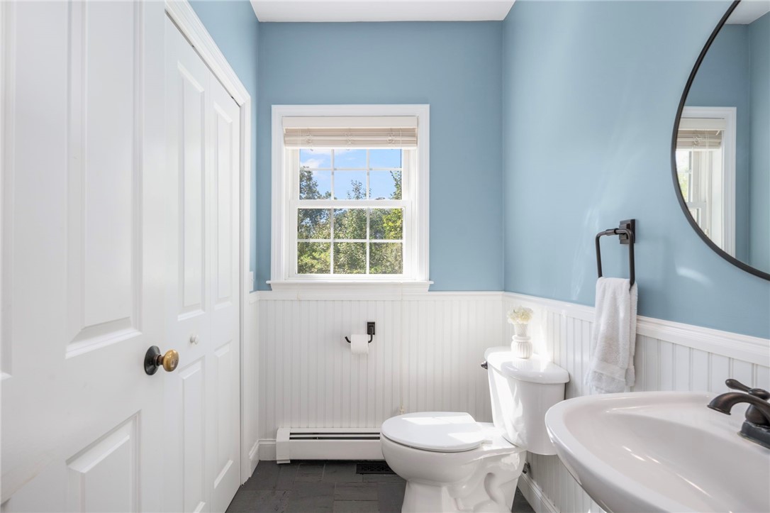 Bathroom with blue walls, white wainscoting, a toilet, and a sunlit window.