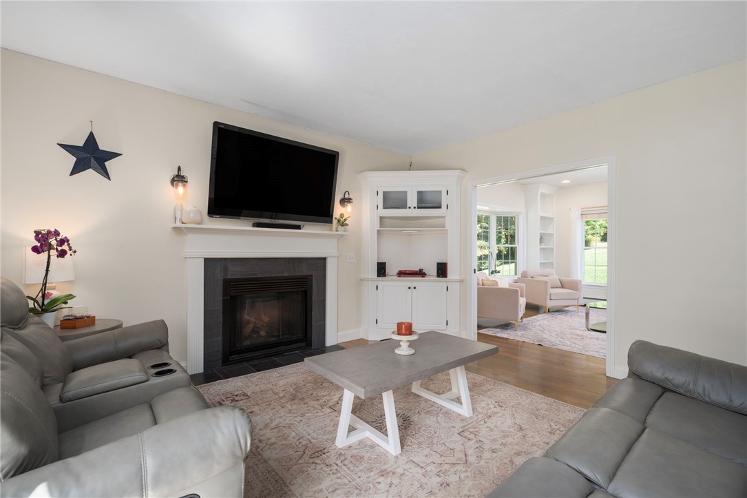 Living room with a fireplace, built-in cabinets, gray leather sofas, and a doorway to a bright sitting room.