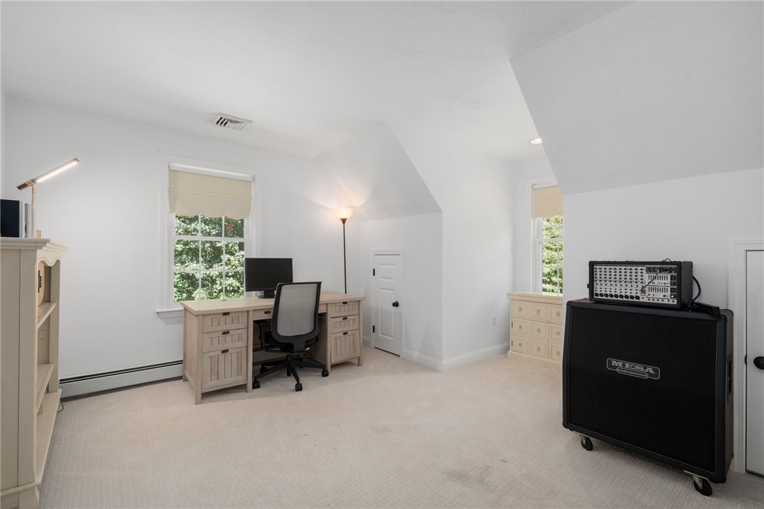 Carpeted home office with a desk beneath a window and a large guitar amplifier.
