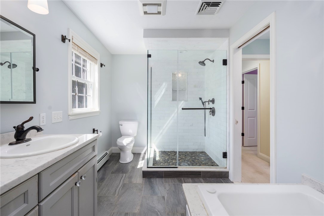 Bright bathroom with a glass-enclosed shower, gray vanity, and soaking tub.