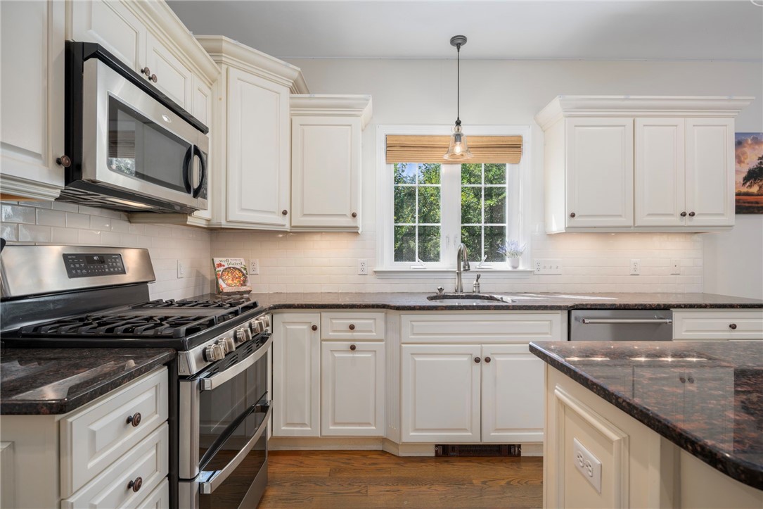 Kitchen with white cabinetry, dark stone counters, stainless steel appliances, and a window over the sink.