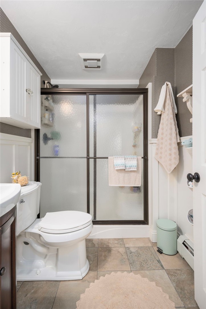 Bathroom with a frosted-glass shower, white toilet, and stone-look tile floor.