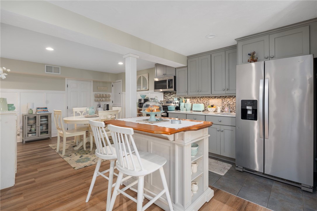 Kitchen with gray cabinets, a stainless steel refrigerator, and a wood-topped island beside the dining area.