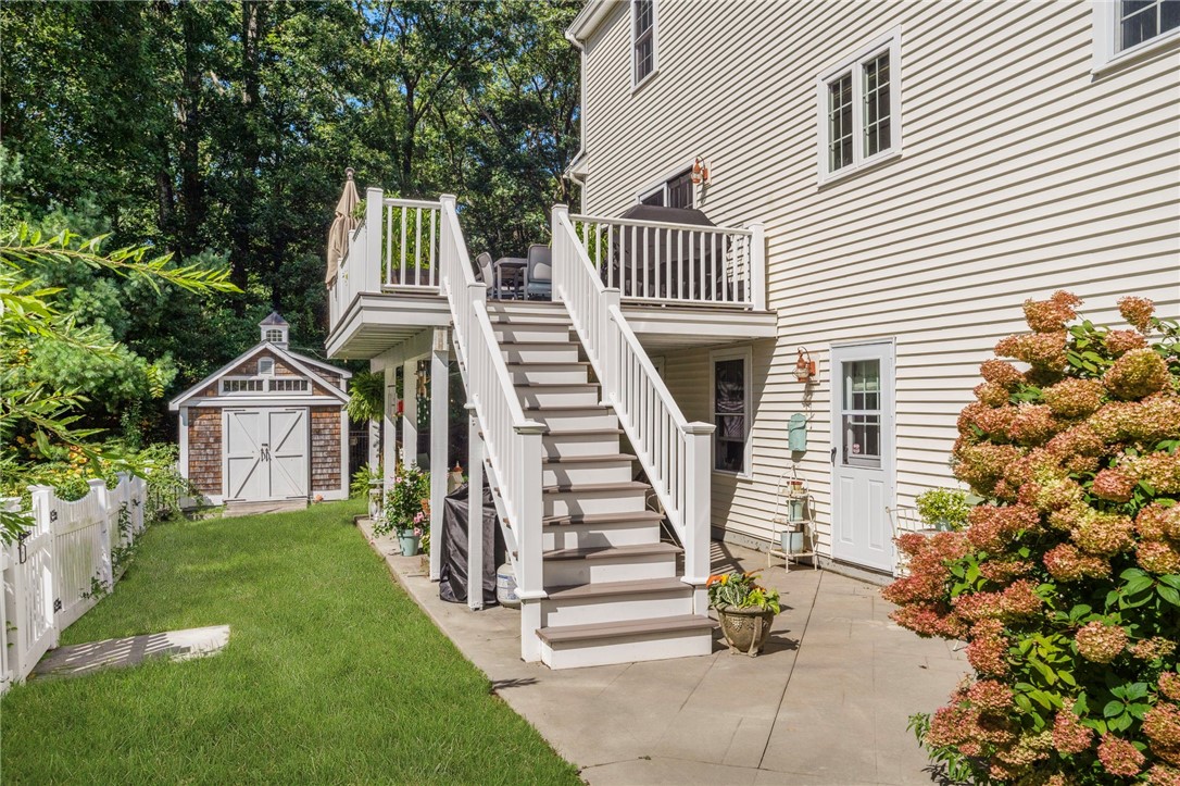 House with elevated white deck and stairs, a paved patio, and a lawn beside a garden shed.