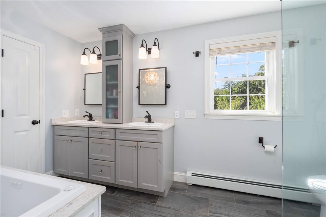 Bathroom with a double-sink vanity, tall storage cabinet, soaking tub, and glass shower.