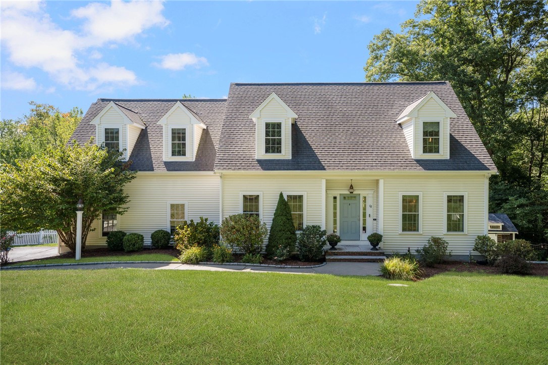 White two-story home with a steep shingled roof, dormer windows, and a landscaped front lawn.