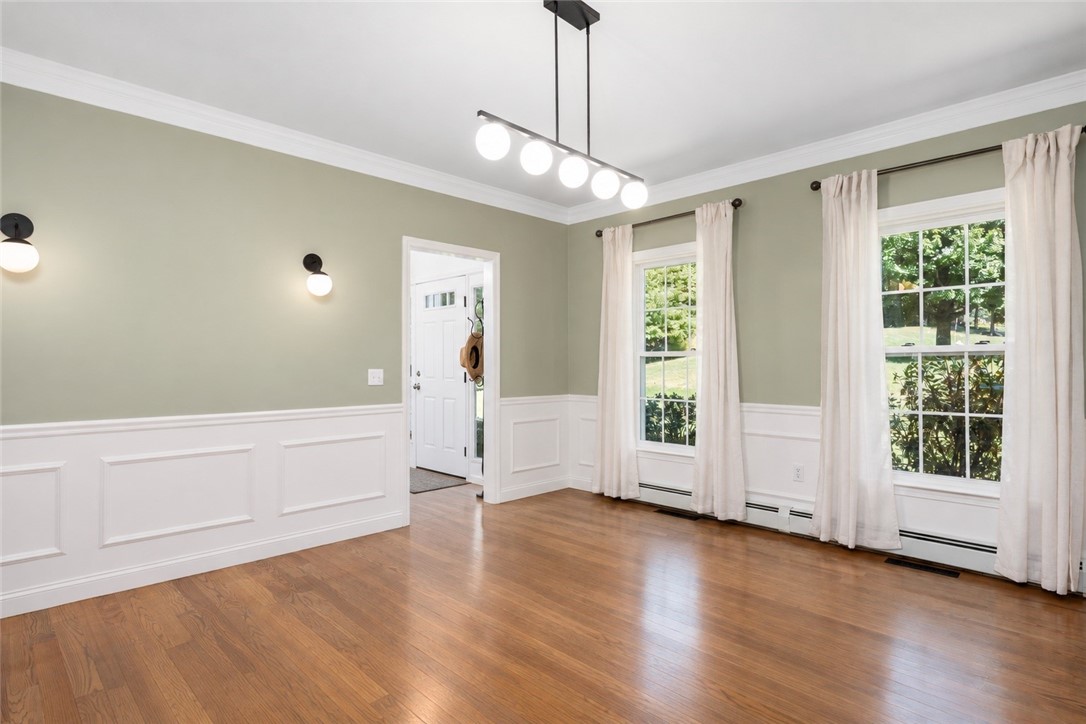 Empty dining room with hardwood floors, paneled wainscoting, and tall curtained windows.