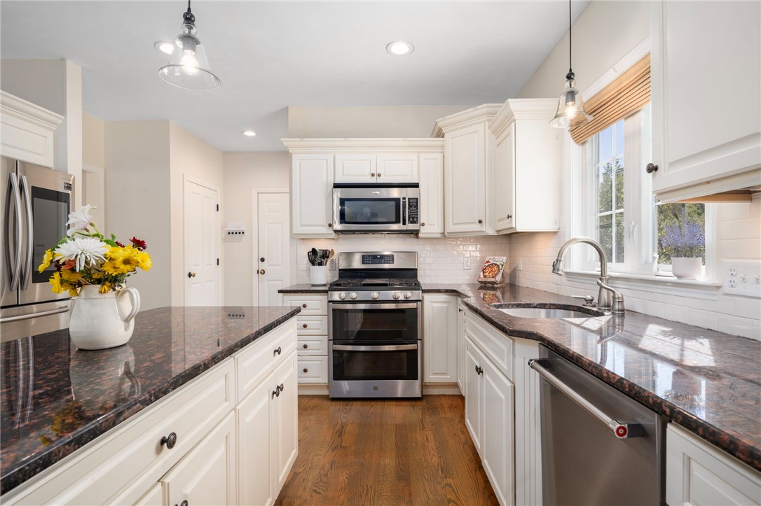 Bright kitchen with white cabinets, granite counters, stainless steel appliances, and hardwood floors.