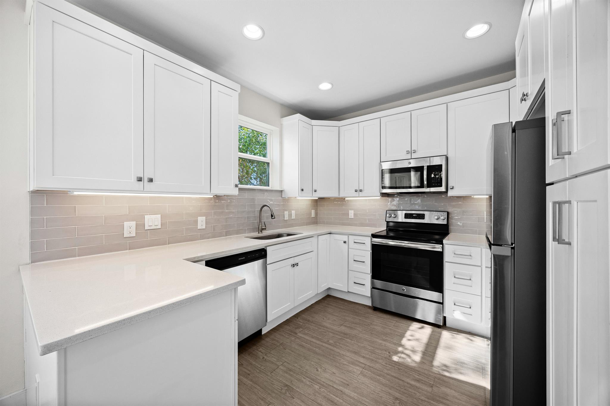 Kitchen with white cabinets, stainless steel appliances, gray tile backsplash, and wood-look flooring.