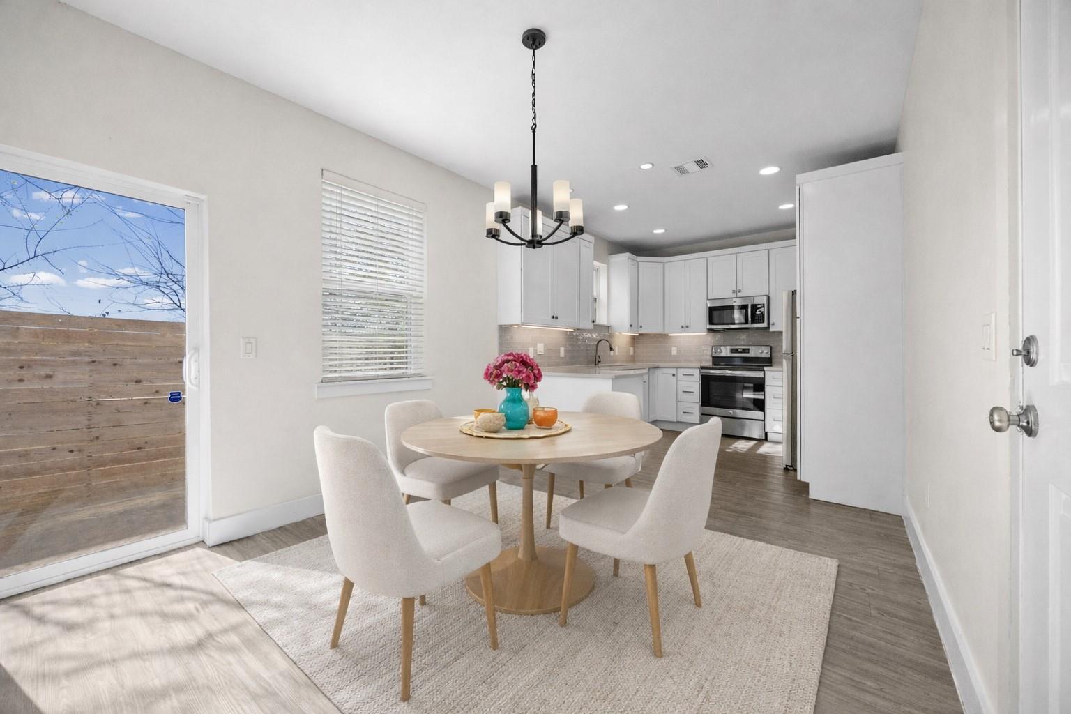Staged dining area with round table and upholstered chairs beside a bright white kitchen.