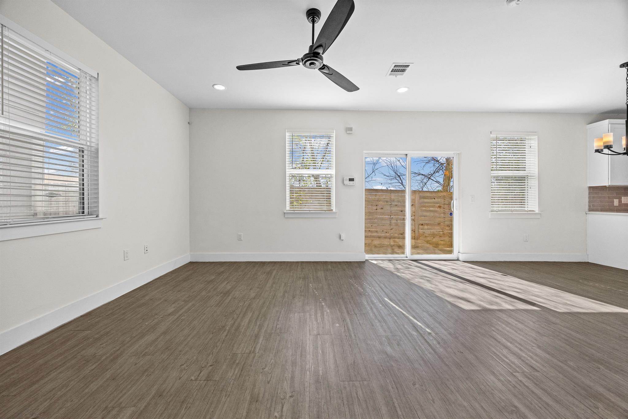 Vacant living room with wood-look floors, ceiling fan, and sliding glass doors to a fenced patio.