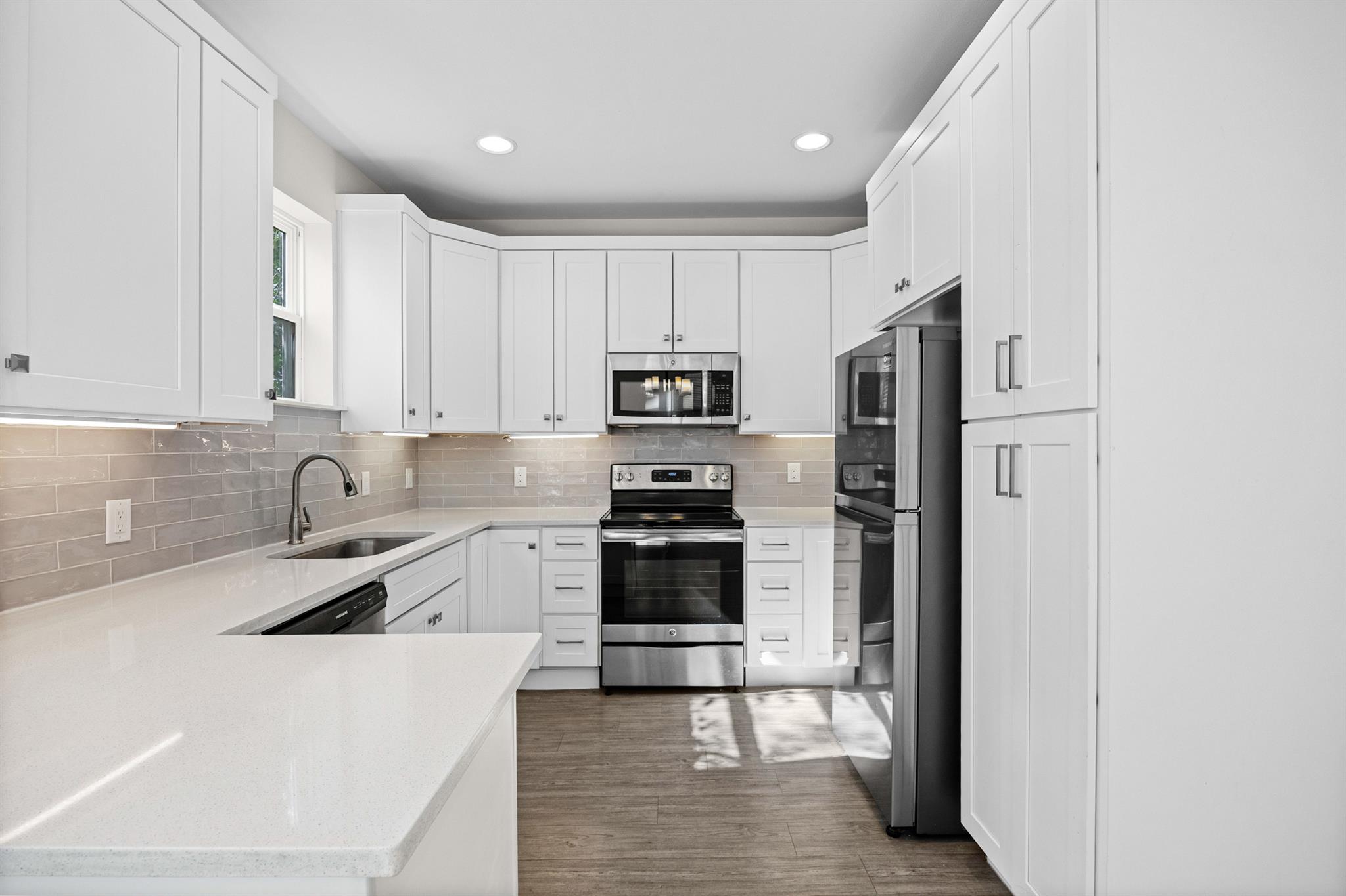 Kitchen with white cabinets, stainless steel appliances, gray tile backsplash, and a broad peninsula counter.