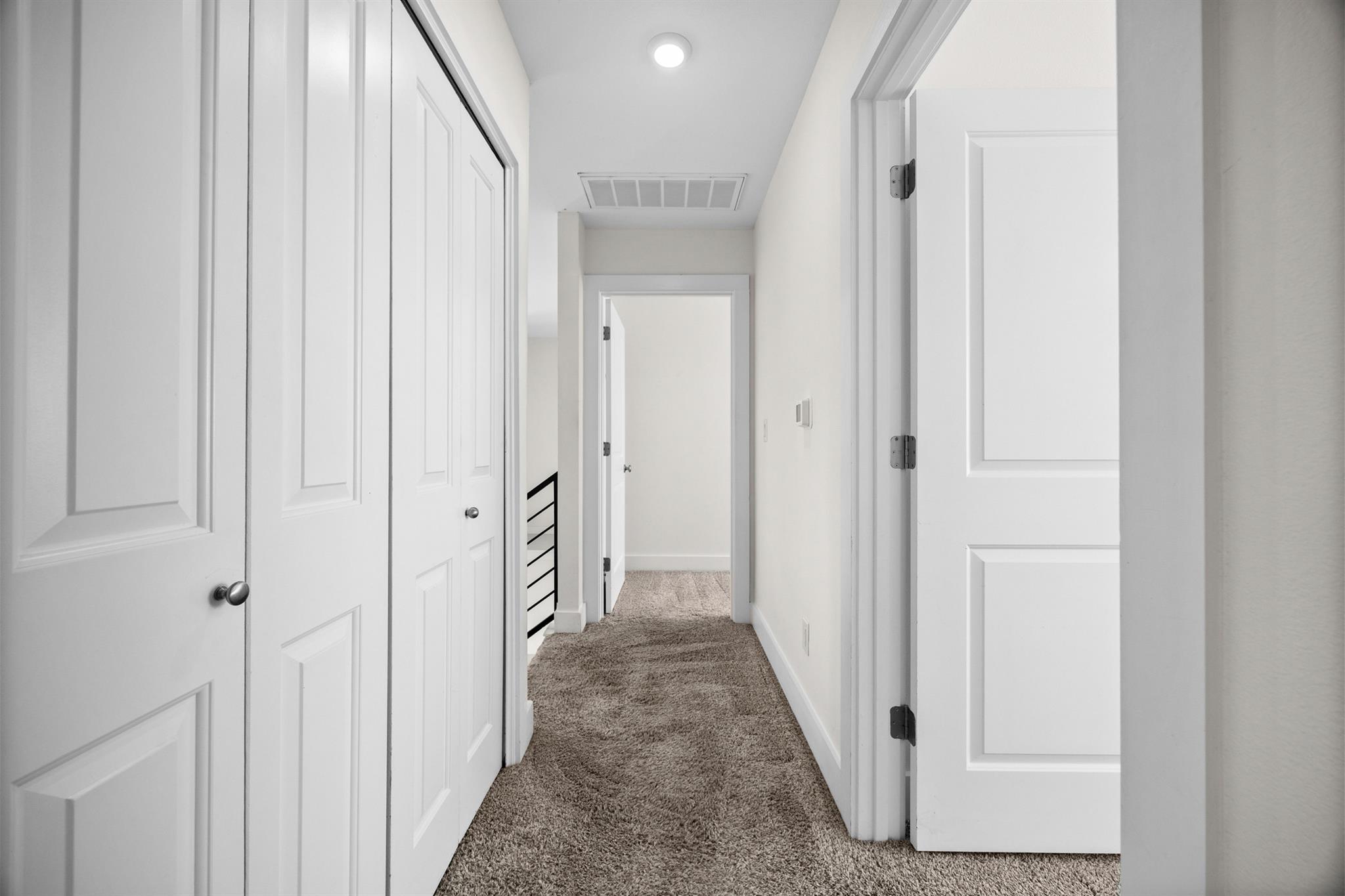 Empty carpeted hallway with white paneled doors along both sides.