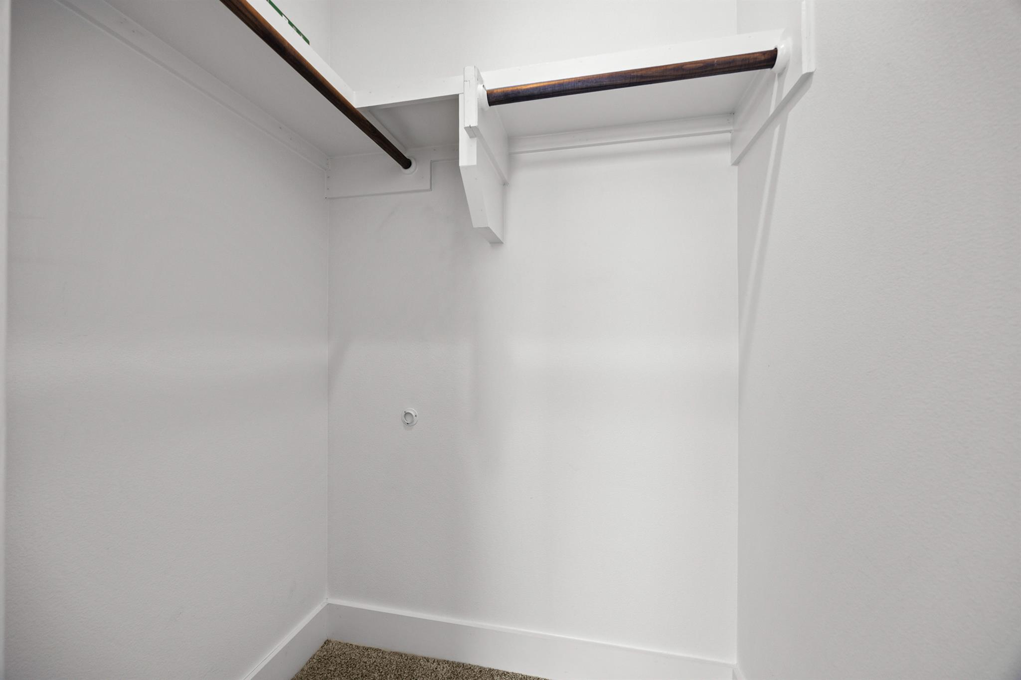 Empty white closet with carpeted floor, built-in shelves, and dark wood hanging rods.