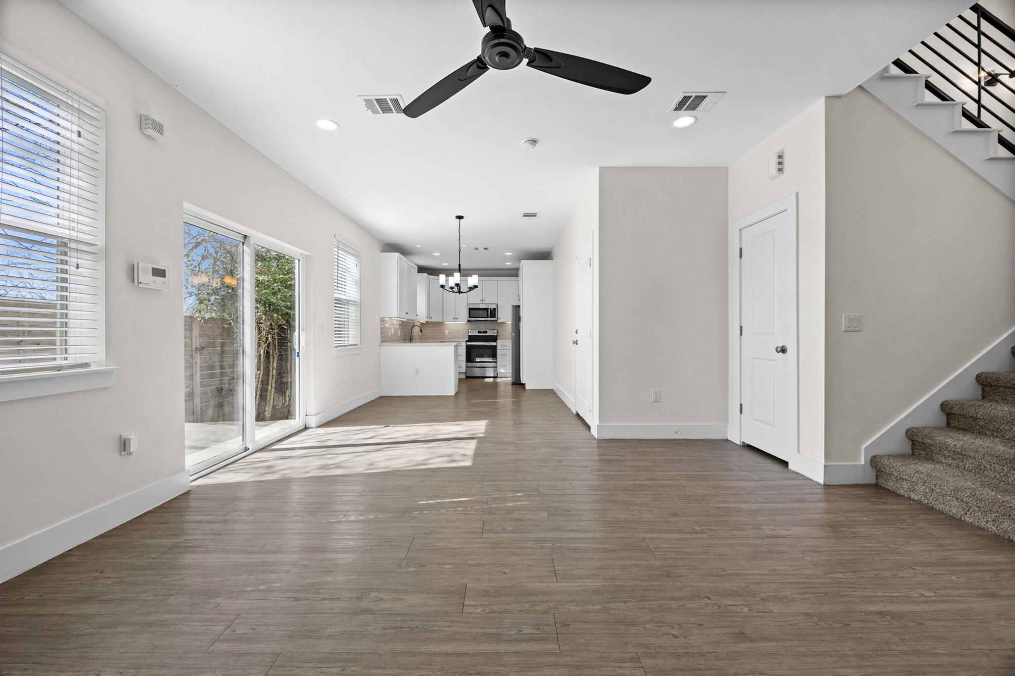 Open living area with wood-look floors, sliding glass doors, a white kitchen, and carpeted stairs.