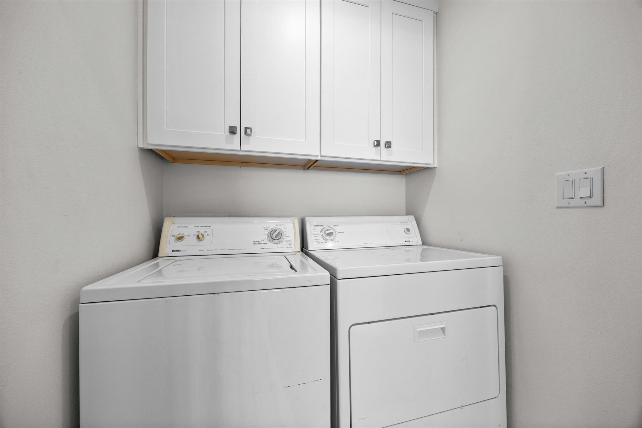 Laundry area with a white washer and dryer beneath overhead cabinets.