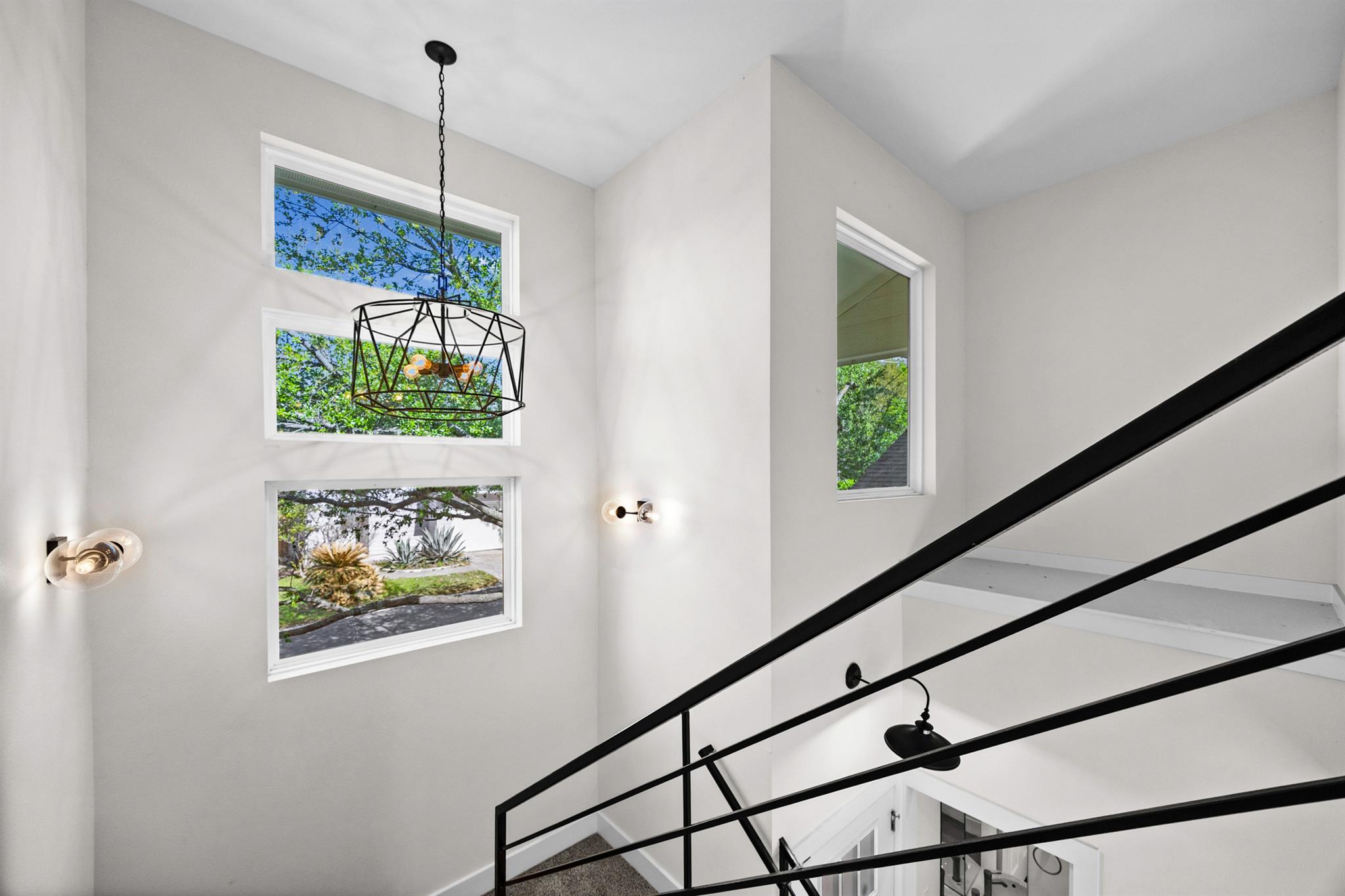 Double-height stairwell with black metal railings, stacked windows, and a geometric pendant light.