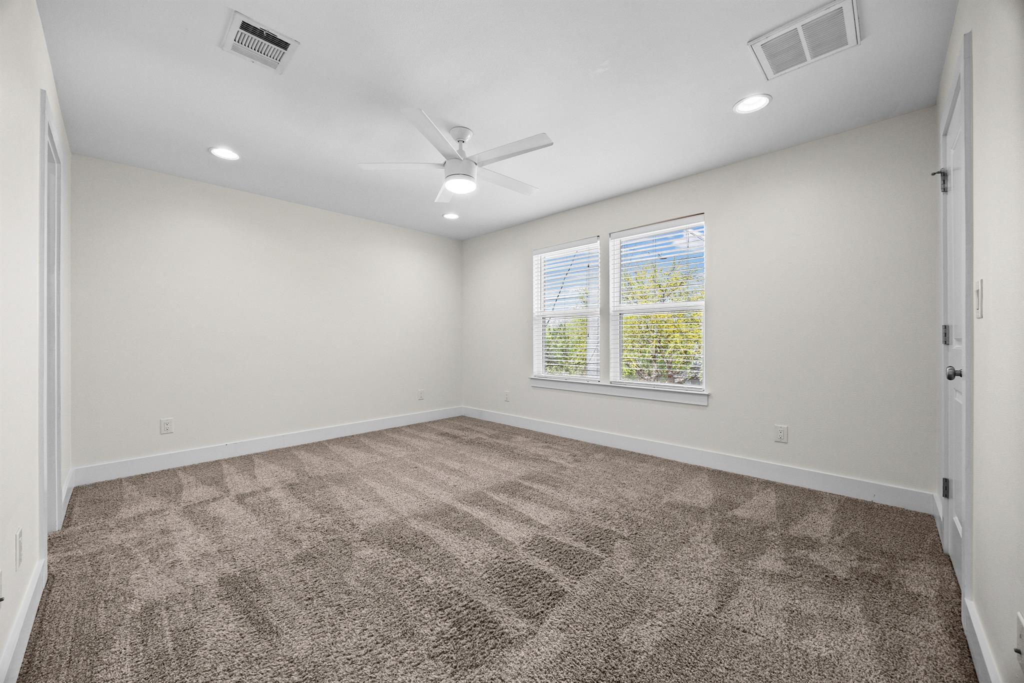 Empty carpeted bedroom with two windows and a ceiling fan.