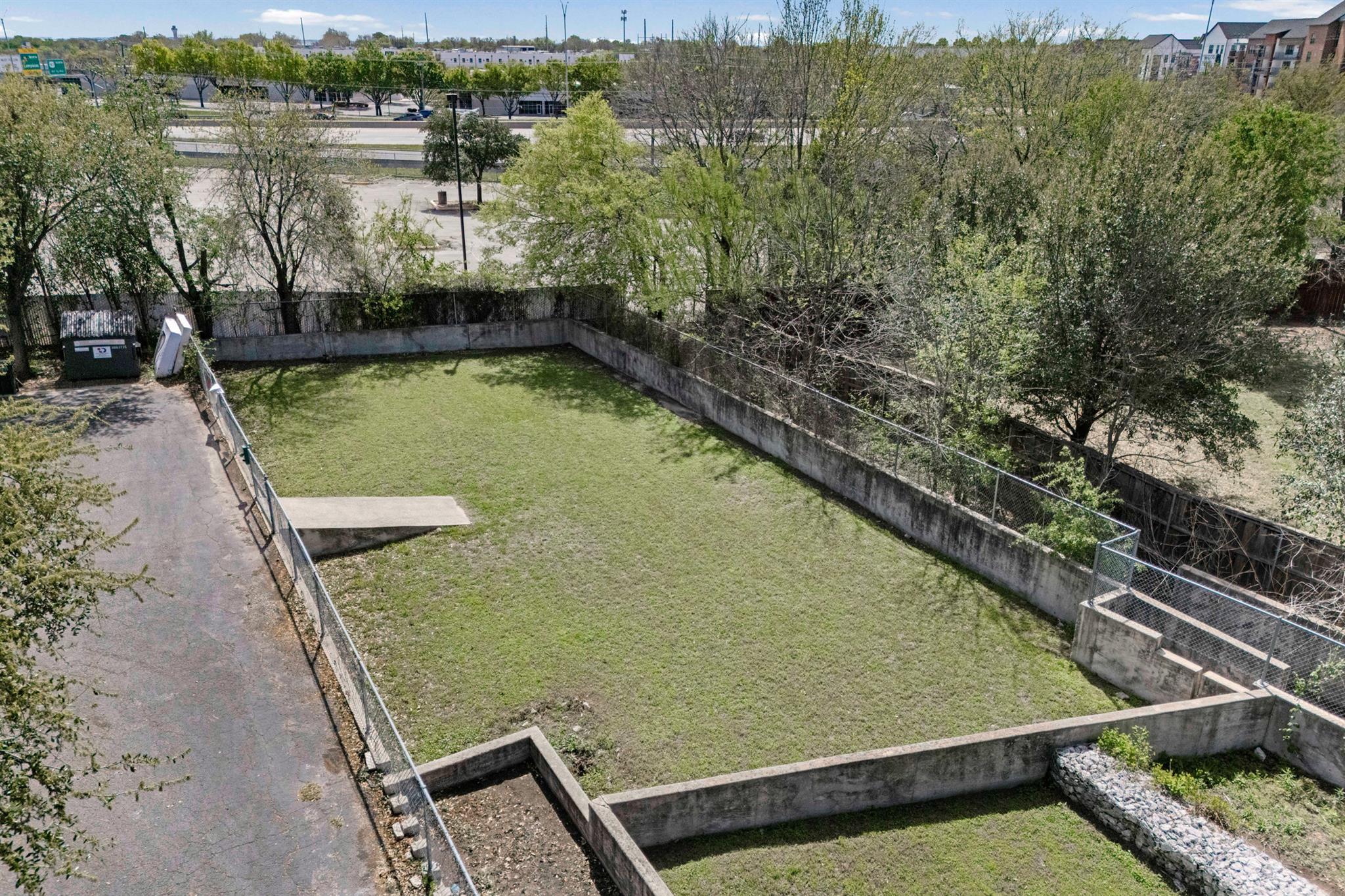 Grassy fenced yard with concrete retaining walls and a paved lane alongside.